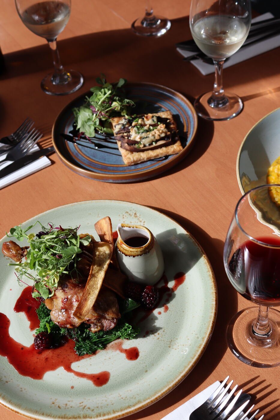 A main course with dark greens, blackberries and a red wine sauce, served on a pale green plate beside a glass of red wine